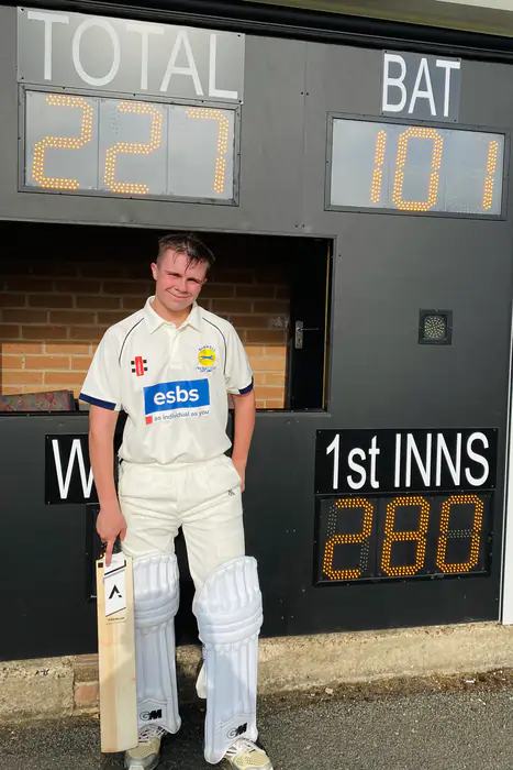 Cricketer with ANGLAR bat in front of scoreboard, representing Anglar cricket accessories.